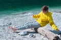 A girl in a yellow hoodie sits on a log by the sea and balances while keeping her legs hanging Royalty Free Stock Photo