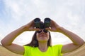 Girl in a yellow jacket looking through binoculars against the sky Royalty Free Stock Photo