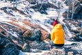 Girl in a yellow jacket and a red knitted hat in nature sits on a stone. rest in the highlands in spring. reflections on life in Royalty Free Stock Photo