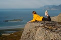 Girl in yellow jacket and sunglasses lies on stone in on the edge of rocks in mountains and looking to fjord Royalty Free Stock Photo