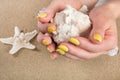 Girl with yellow nails holding big sea shell in hand and starfish on beach sand in background Royalty Free Stock Photo