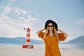 A girl in a yellow-orange suit on the beach against the background of the sea, mountains and a lighthouse. Fashionable woman in