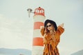 A girl in a yellow-orange suit on the beach against the background of the sea, mountains and a lighthouse. Fashionable woman in