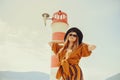 A girl in a yellow-orange suit on the beach against the background of the sea, mountains and a lighthouse. Fashionable woman in