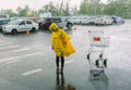 Girl in yellow raincoat stand alone under rain in parking lot. Look down on wet asphalt. Many cars behind. Empty Royalty Free Stock Photo