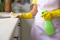The girl in yellow rubber gloves and an apron removes. Hand wipes the table surface and holds the spray Royalty Free Stock Photo