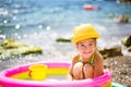 Girl in yellow straw hat plays in outdoor near sea, in water with a bucket in an inflatable pool on the beach. Indelible products Royalty Free Stock Photo
