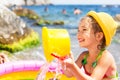 Girl in yellow straw hat plays in outdoor near sea, in water with a bucket in an inflatable pool on the beach. Indelible products Royalty Free Stock Photo