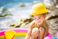 Girl in yellow straw hat plays with the wind, water and a water dispenser in an inflatable pool on the beach. Indelible products Royalty Free Stock Photo