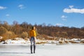 A girl in a yellow sweater with a short haircut stands back on the ice of the river