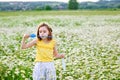 A girl in a yellow T-shirt and a wreath of daisies on her head plays in nature with soap bubbles. A child in a blooming chamomile