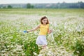 A girl in a yellow T-shirt and a wreath of daisies on her head plays in nature with soap bubbles. A child in a blooming chamomile