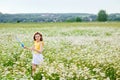 A girl in a yellow T-shirt and a wreath of daisies on her head plays in nature with soap bubbles. A child in a blooming chamomile