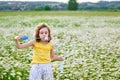 A girl in a yellow T-shirt and a wreath of daisies on her head plays in nature with soap bubbles. A child in a blooming chamomile