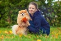 Girl or young woman holding Pomeranian spitz and bouquet of fallen leaves in the park in autumn