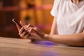 A girl or young woman sits at the table, holds in hands and uses a smartphone to correspond, read and send messages