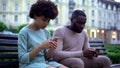 Girlfriend and boyfriend chatting in their smartphones, sitting on bench, ignore Royalty Free Stock Photo