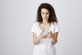 Girlfriend freaked out seeing strange message in boyfriend phone. Portrait of confused bothered young woman with curly