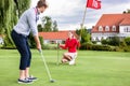 Girlfriend looking at male golfer putting the ball in green Royalty Free Stock Photo