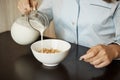 Girlfriend preparing simple breakfast in morning. Cropped shot of woman in nightwear pouring milk in bowl with cereals Royalty Free Stock Photo