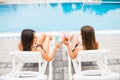 Girlfriends clinking glasses with cocktails at lounge at the poolside in summer Royalty Free Stock Photo