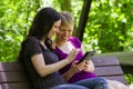 Girlfriends sharing an etablet on park bench, horizontal