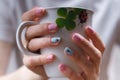 Girlish manicure with volumetric ladybugs on pink and blue fingernails. Female hands holding a cup with lady-bird and clover leaf