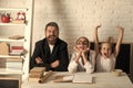 Girls and bearded man sit at desk with books
