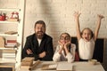 Girls and bearded man sit at desk with books