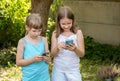 Girls children holding their smartphones in hands, kids outdoors looking at their mobile phones laughing, using technology, apps, Royalty Free Stock Photo