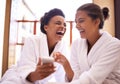 Girls day at the spa. two friends in bathrobes using a cellphone at a spa. Royalty Free Stock Photo