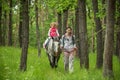 Girls enjoying horseback riding in the woods with mother, young pretty girls with blond curly hair on a horse, freedom Royalty Free Stock Photo