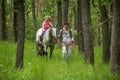 Girls enjoying horseback riding in the woods with mother, young pretty girls with blond curly hair on a horse, freedom Royalty Free Stock Photo