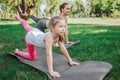 Girls are excercising outside in park. They are stretching their left legs and leaning on both hands and right legs