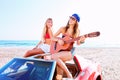 Girls having fun playing guitar on th beach in a car Royalty Free Stock Photo