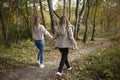 The girls are holding hands. Friends are walking in the autumn forest. Two girls happily walk through the park. Royalty Free Stock Photo