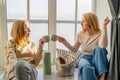 girls holding hot cups of coffee drinking, sitting near the window and looking at each other sharing funny things Royalty Free Stock Photo
