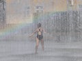 A girls joyfully runs and bathes in the city`s fountain in the rays of the rainbow. Hot sunny weather. Children`s carefree game in