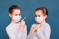 Girls in medical masks look at a syringe with medicine in their hands and are afraid. Vaccination, treatment of children.