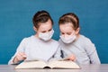 Girls in medical masks in quarantine carefully read a book at the table. Education children in isolation in an epidemic