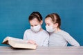 Girls in medical masks in quarantine are reading a book at the table. Education children in isolation in an epidemic