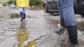 girls in raincoats and rubber boots walk along road flooded with torrential rains, their feet walk through puddles city