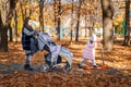 girls ride scooters in the autumn city park, happy children walk together with a baby carriage, beautiful nature, bright sunny day Royalty Free Stock Photo