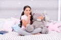 Girls secret. Cute kid show silence finger gesture. Little secret. Small girl play with teddy bear in bed. Keeping mouth