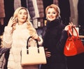 Girls with smiling faces in black and white fur coats hold purses in hands. Luxury style concept. Women with blond hair Royalty Free Stock Photo