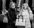 Girls with smiling faces in black and white fur coats hold purses in hands. Luxury style concept. Women with blond hair Royalty Free Stock Photo