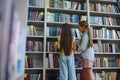 Girls standing near the high book shelves in the school library Royalty Free Stock Photo