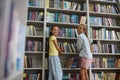 Girls standing near the high book shelves in the school library Royalty Free Stock Photo