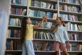 Girls standing near the high book shelves in the school library Royalty Free Stock Photo