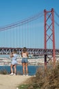 Girls taking a photography with her smartphone of the panorama of the famous 25th April suspension bridge on the tagus river